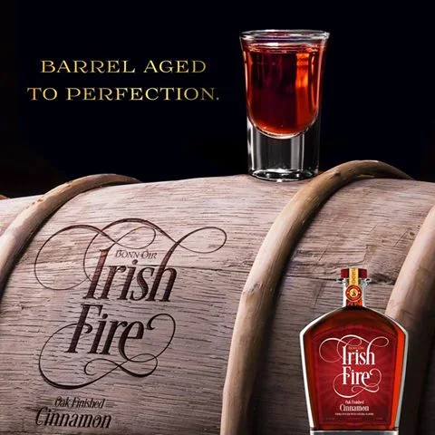 A shot of Irish Fire on an oak barrel branded with the Irish Fire logo, beside a bottle. Text reads Barrel aged to perfection.